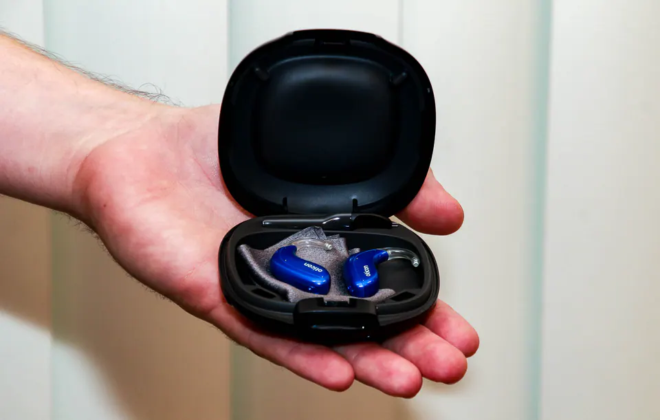 An open hearing aid charging case resting in the palm of a hand