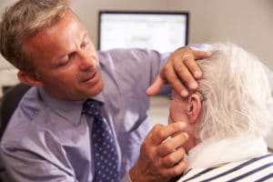 Doctor fitting a senior female patient with a hearing aid